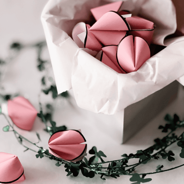 Rosa Glückskekse aus Papier in einer weißen Geschenkbox mit Kleeblatt-Dekoration.