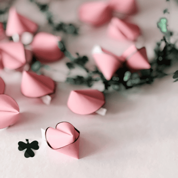 Selbstgemachte rosa Glückskekse aus Papier mit kleinen Kleeblättern als Silvester-Mitbringsel.